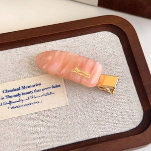 Detailed macro view of pink marble acetate hair clip with golden metal base and logo