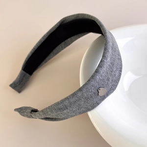 Close-up of a wide grey cotton headband with a small silver heart-shaped pendant