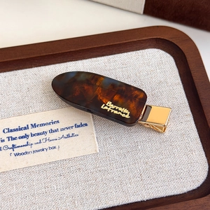 Detailed close-up of a tortoiseshell acetate hair clip with a gold logo on wood