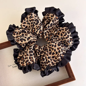 Leopard print satin scrunchie with black lace trim on a minimalist wooden display