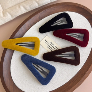Détail de pinces à cheveux triangulaires en velours coloré sur un plateau en bois