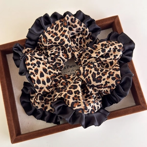 Detail of leopard print scrunchie with black satin ruffled edge on velvet tray