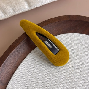 Détail de la barrette en velours jaune moutarde sur fond vintage en bois et lin