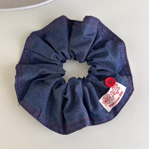 Detail view of denim scrunchie with red stitching, vintage button and woven brand label
