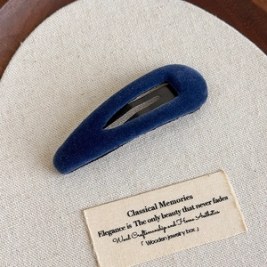 Vue détaillée d'une pince à cheveux en velours bleu foncé sur fond de tissu texturé