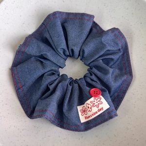 Close-up of denim hair scrunchie with red stitching, button, and Have a nice day label