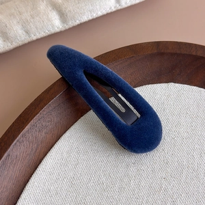 Détail d'une pince à cheveux en velours bleu foncé sur un plateau en bois mat