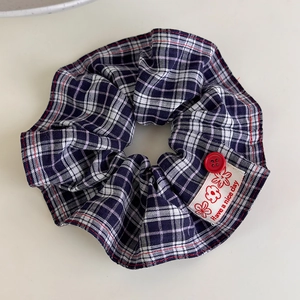 Detail of checkered fabric scrunchie with red button and 'Have a nice day' label