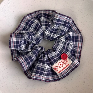 Close-up of blue and red plaid hair scrunchie with red button and Have a Nice Day tag