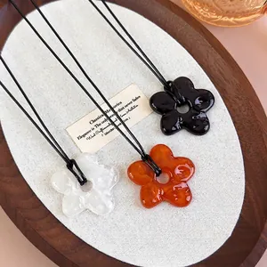Trois colliers à pendentif fleur en acrylique noir, ambre et blanc sur plateau