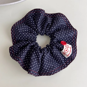 Detail of navy blue polka dot scrunchie with red button and Have a nice day woven label
