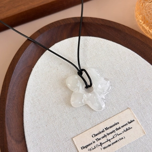 Détail d'un collier pendentif fleur en acrylique avec cordon noir sur lin