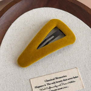 Détail d'une pince à cheveux triangulaire en velours jaune moutarde sur fond rétro