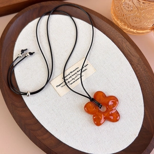 Détail macro du pendentif fleur en résine ambrée sur collier en cordon noir sur plateau