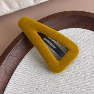 Détail d'une pince à cheveux triangulaire en velours jaune moutarde sur un plateau