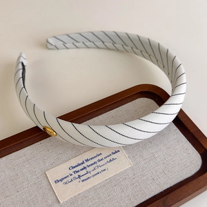Gros plan d'un serre-tête rembourré blanc à rayures noires et plaque dorée Hand Made