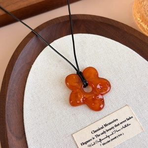 Gros plan du pendentif fleur en acrylique ambre avec texture marbrée sur cordon noir