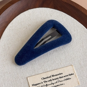 Détail de la pince à cheveux triangle en velours bleu marine sur une surface texturée