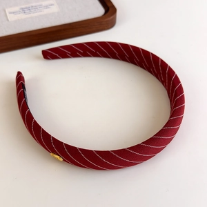 Détail du serre-tête en tissu rayé bordeaux avec emblème doré et doublure antidérapante