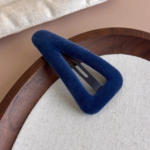 Détail d'une pince à cheveux triangulaire en velours bleu marine sur plateau en bois