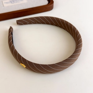 Détail de l'étiquette dorée sur le serre-tête rayé marron avec texture tissée