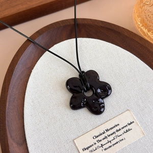 Gros plan d'un pendentif fleur noire sur un collier minimaliste en cordon noir