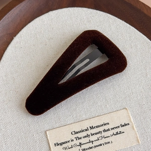 Détail de la pince à cheveux triangulaire en velours marron sur un plateau en bois