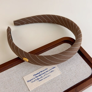 Détail d'un serre-tête en tissu sergé marron avec une plaque dorée gravée 'Handmade'