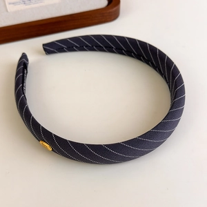 Détail macro d'un serre-tête en tissu rayé avec une plaque en métal dorée Hand Made