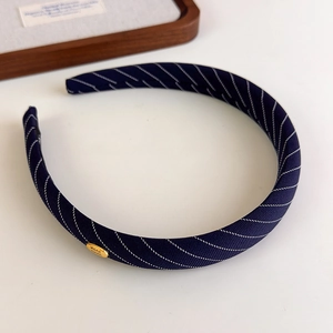 Détail d'un serre-tête en tissu rayé bleu marine avec logo métallique doré fait main