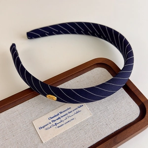 Détail d'un serre-tête en tissu à rayures bleu marine avec logo doré fait main