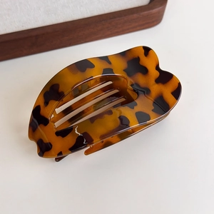 Detail of a large leopard print claw clip with heart-shaped edges on a wooden tray