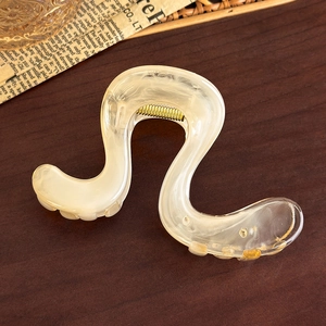 Macro detail of cream wavy hair claw clip with marble texture on dark wood background