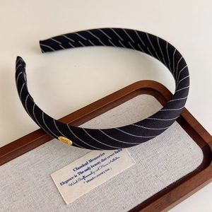 Gros plan d'un serre-tête en tissu rayé noir avec petit logo métallique doré chic
