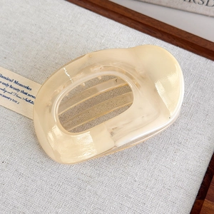Detail of a large cream acetate hair claw clip with marble texture on grey linen