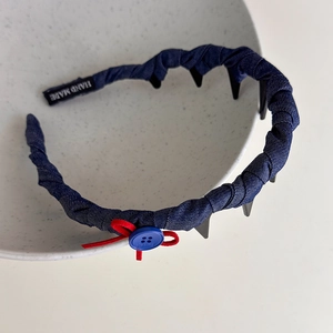 Close-up of blue denim headband with red bow, handmade button, and interior teeth