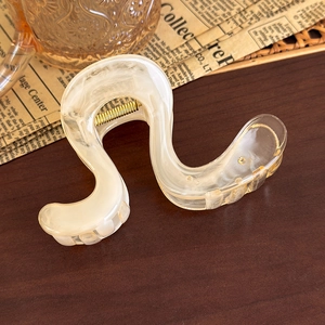 Close-up of S-shaped amber gradient hair claw clip with golden metal spring detail