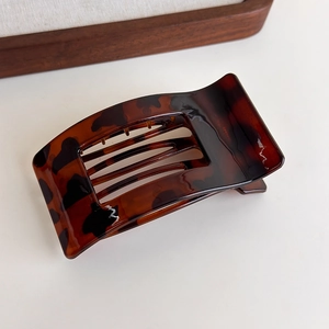 Macro detail of tortoiseshell pattern hair claw clip with high gloss finish on wooden surface