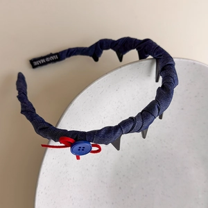 Detail of navy denim headband featuring red string bow and a blue button detail