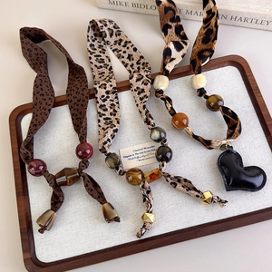 Detail of leopard print scarf necklaces with amber resin beads in a rustic wooden tray