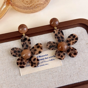 Detail of leopard print flower earrings with resin texture on a wooden tray
