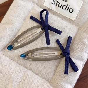 Detail of two denim bow hair clips with blue rhinestones on a beige quilted surface
