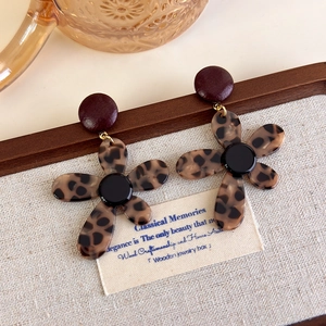 Macro shot of retro leopard print floral earrings on a beige canvas display background