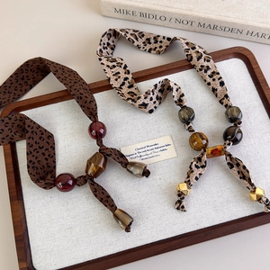 Detail view of leopard print silk scarf necklaces with amber beads and vintage charms