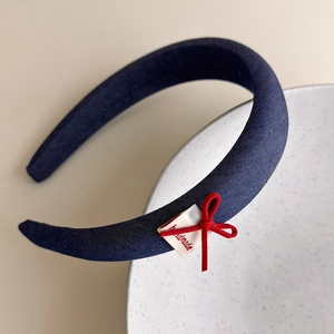 Detail of navy blue plaid headband featuring a red bow and a white handmade fabric label