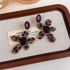 Close-up of leopard print flower earrings on a vintage wooden tray and linen cloth