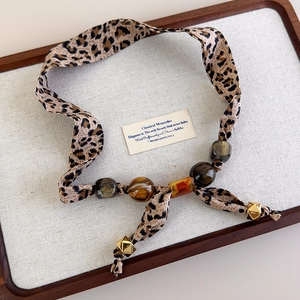 Detail view of leopard print silk scarf necklace with amber resin beads and gold accents