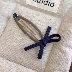 Detail of khaki snap hair clip with a navy denim bow and square blue rhinestone crystal
