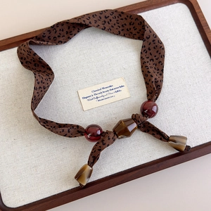 Detail of leopard print fabric necklace with glossy dark red and brown beads