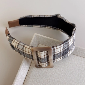 Detail view of the brown plaid headband featuring a textured resin square buckle on top